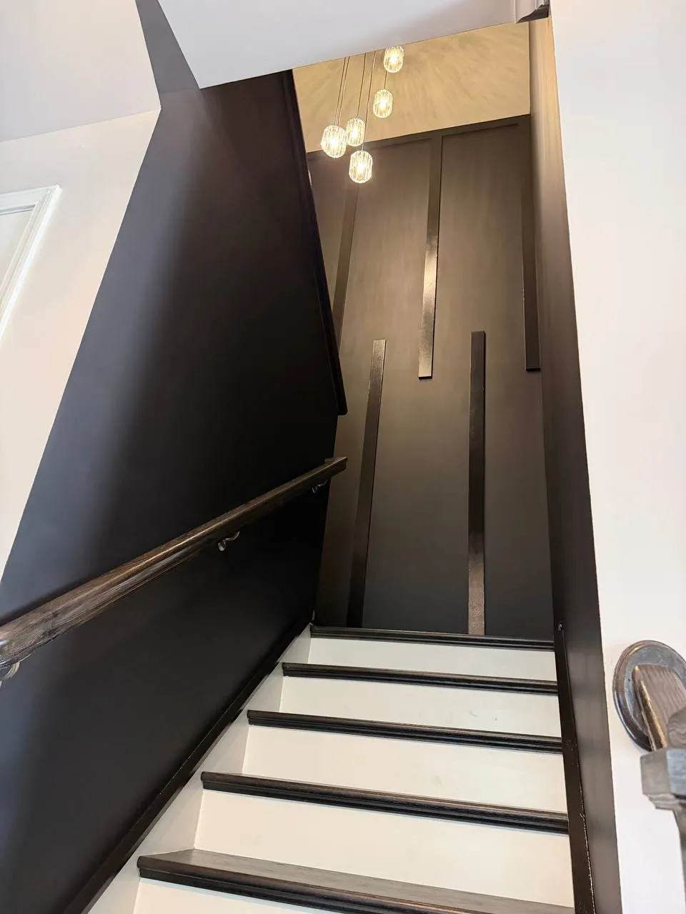 Black slat accent wall rising along a staircase under pendant lights