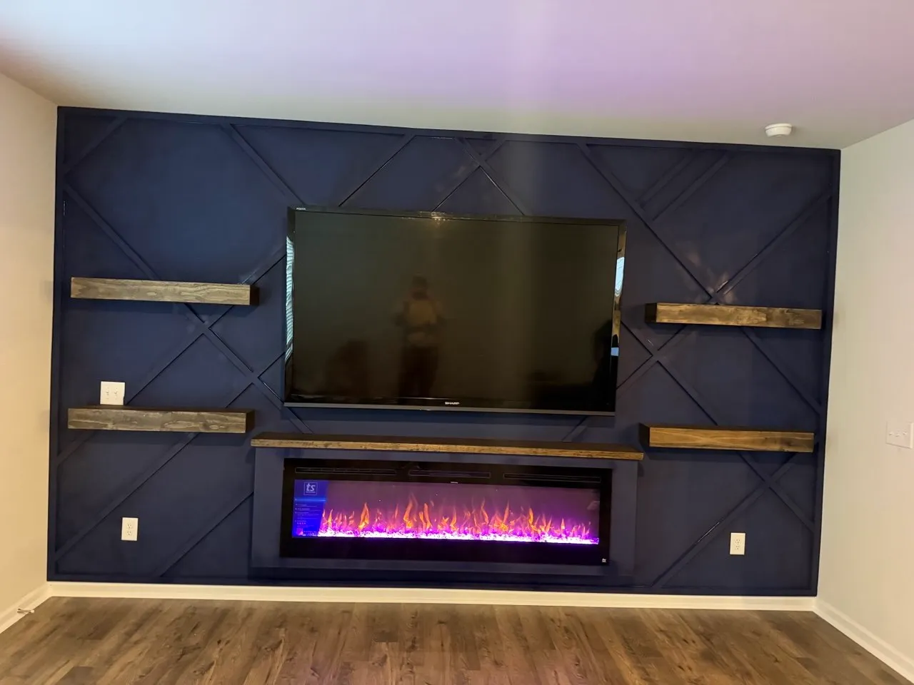 Navy geometric accent wall with floating wood shelves, a TV and an electric fireplace