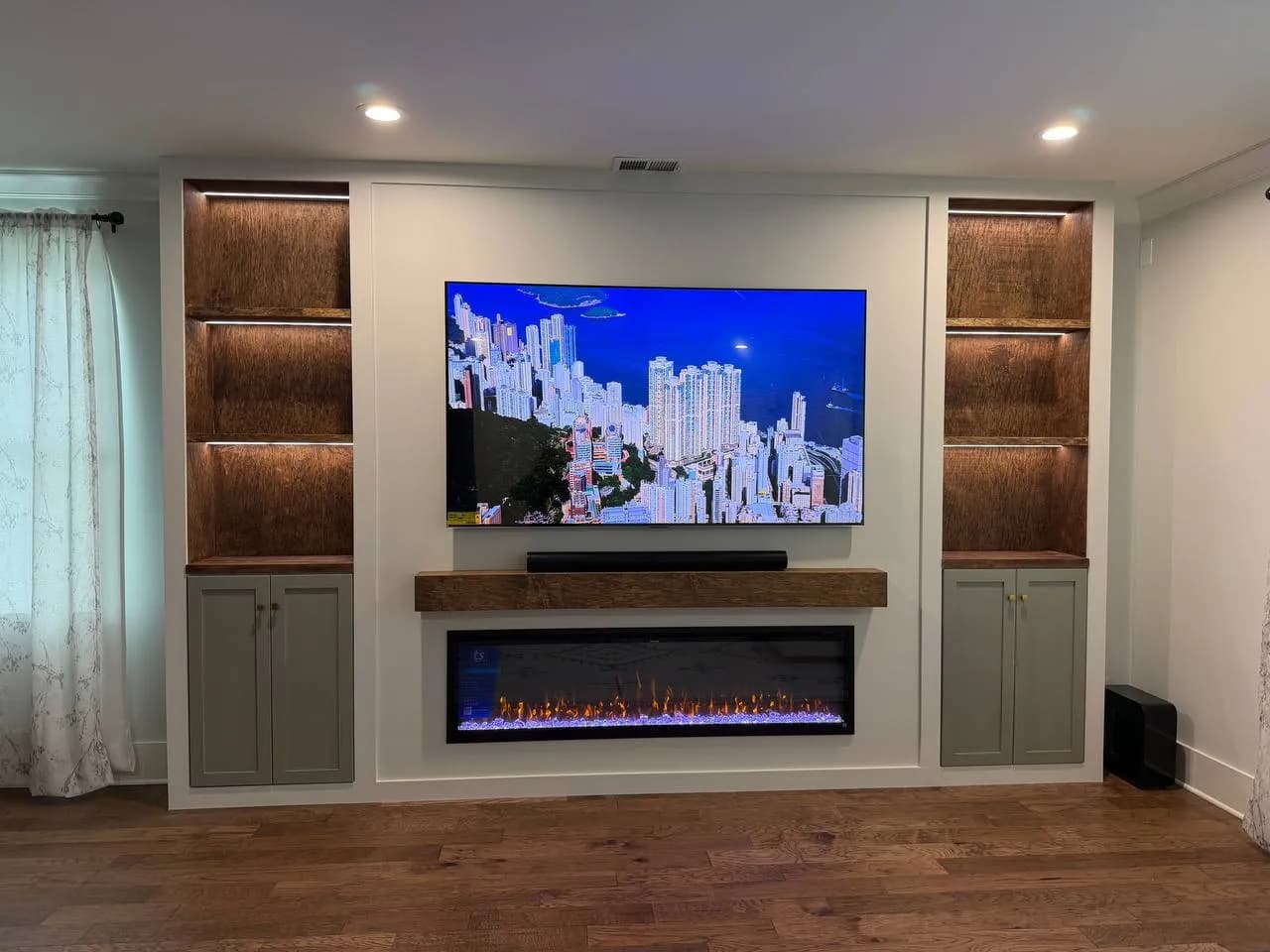 Media wall with lit wood shelves and painted cabinets on both sides of the TV and fireplace