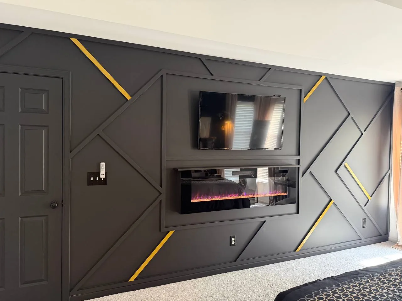 Charcoal geometric accent wall with gold inlays around a TV and electric fireplace