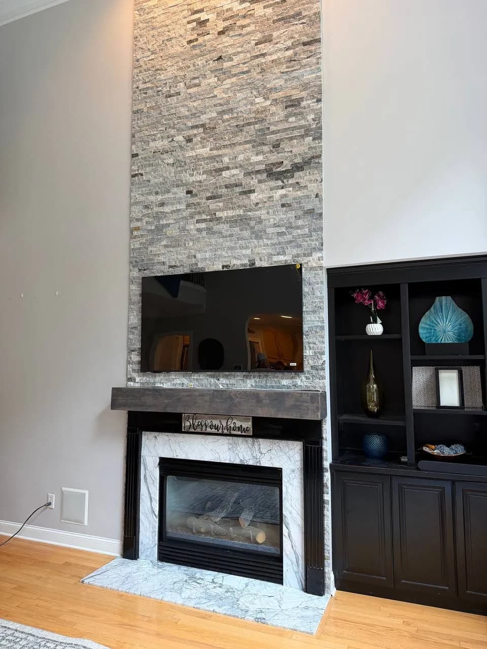 Stacked stone media wall with a TV above a gas fireplace and dark built-in cabinets beside it